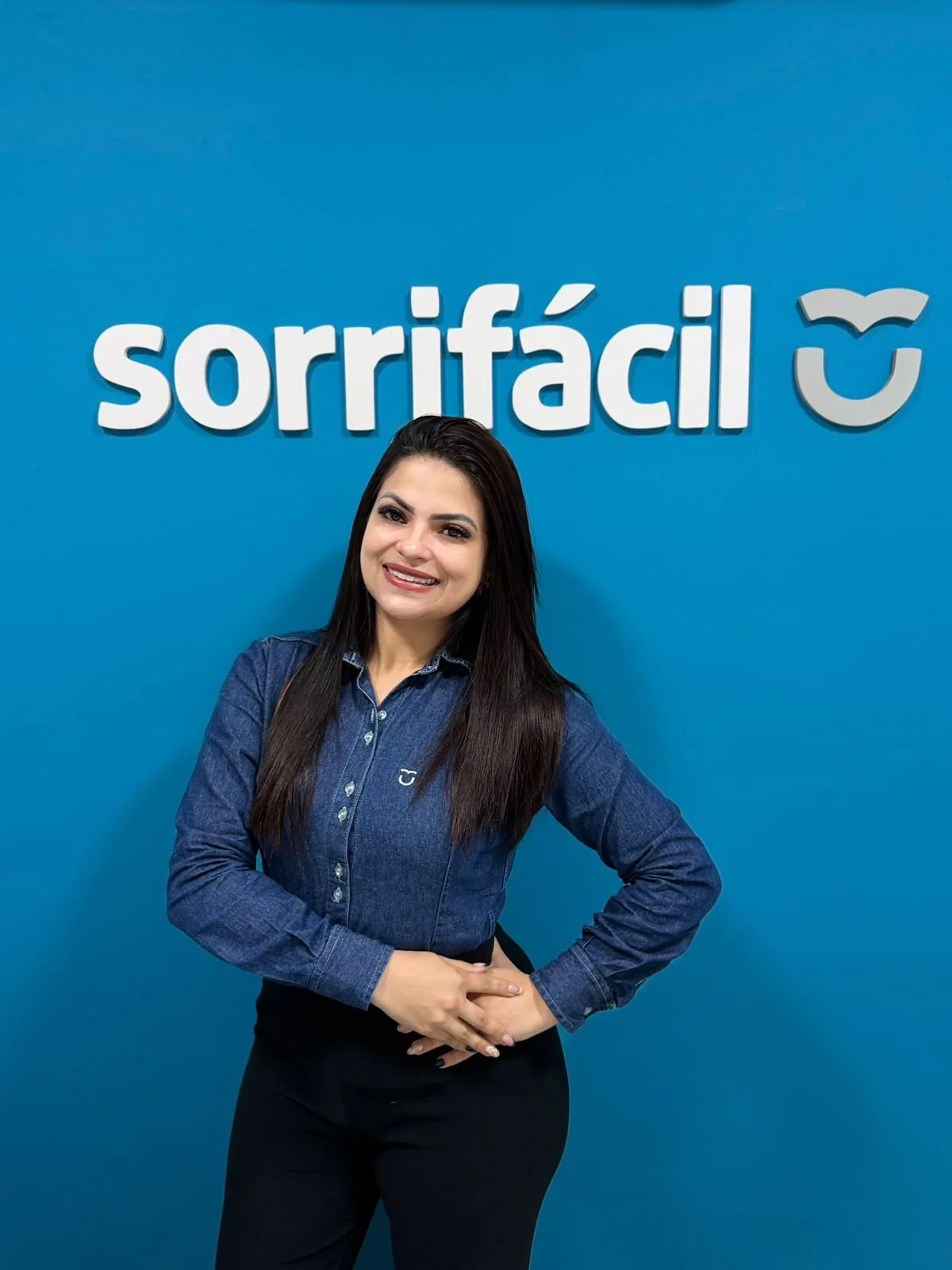 Integrante da equipe da Sorrifácil Jaguarão sorrindo em frente ao logo da clínica
